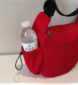 Detail view of red canvas crossbody bag showing functional drawstring side pocket and strap