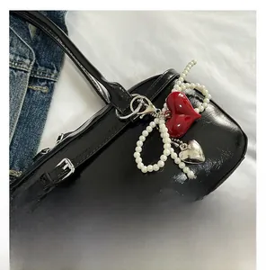 Detailed close-up of a red heart pendant with pearl chain charm on a black leather bag