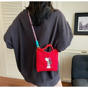 Close-up of red canvas bag with dog embroidery and colorful woven shoulder strap details