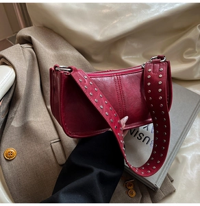 Detail shot of a red leather bag featuring stylish silver studs on a wide shoulder strap