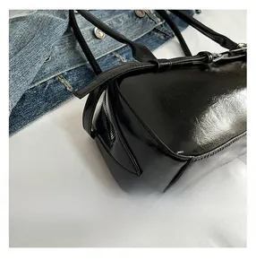 Detail of the polished black leather bag showing the zipper and metal strap buckle
