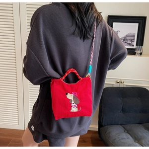 Detail of red crossbody bag with cartoon dog embroidery and woven shoulder strap