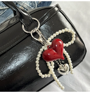 Close-up of heart charm with red glossy heart, silver mini heart and pearls on a black bag