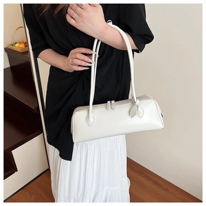 Modern white leather baguette bag worn by a model in a warm indoor setting