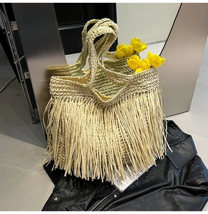 Detail shot of the woven straw tote bag featuring long fringes and sturdy double handles
