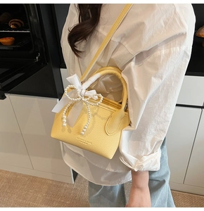 Detail of yellow lychee grain leather bucket bag with pearl bow and ribbon charm