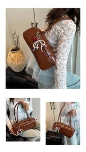 Detail view of brown shoulder bag featuring red heart and pearl bow charms on synthetic leather