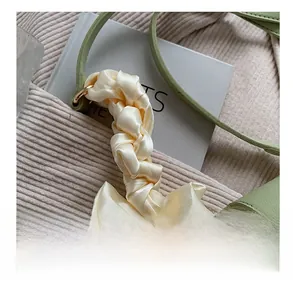 Detail showing creamy satin bow scarf accessory on light green leather crossbody bag