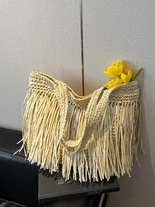 Large beige woven straw tote bag with long fringe tassels and summer beach style