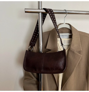 Detail of broad shoulder strap with silver rivets on a brown faux leather baguette bag