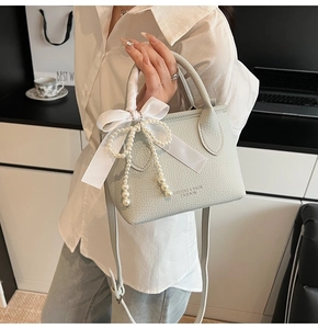 Detail of light green pebbled leather bag with a silk bow and pearl tassel accessory