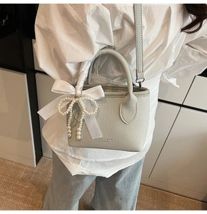 Detail of grey pebble leather handbag with silk bow and elegant pearl charm on white outfit