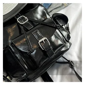 Detail showing shiny black faux leather backpack with silver buckle and flap closure