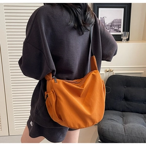 Detailed view of bright orange nylon crossbody bag with adjustable strap and side drawstring