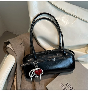 Detail of black glossy wrinkled leather handbag with red heart pearl charm and zipper