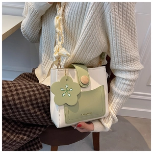 Detail of a chic cream and green crossbody bag with a floral charm and silk woven strap