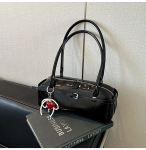 Detail of black glossy shoulder bag with silver buckle and pearl heart charm accessory
