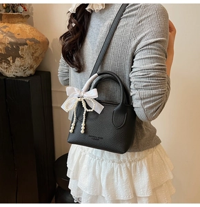 Detail of black lychee grain bucket bag featuring pearl bow charm and silk ribbon decor