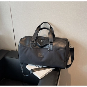 Close-up of a black canvas travel bag with leather accents on a leather sofa