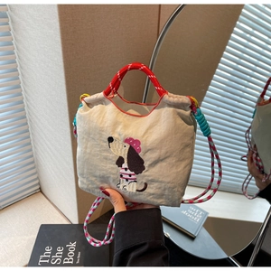 Close-up of cream canvas bucket bag with dog embroidery and colorful woven strap