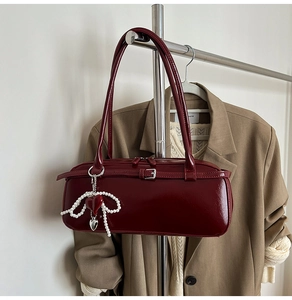 Detail view of burgundy patent leather underarm bag with pearl butterfly and heart charm