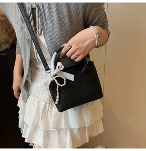 Detail of black pebbled leather handbag featuring white satin bow and pearl charms