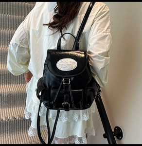 Detail of black PU leather backpack with flip cover, pin buckle, and white logo badge