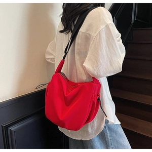 Model wearing a large red nylon dumpling crossbody bag with adjustable black strap