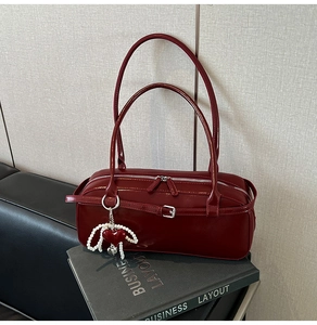 Detail of burgundy glossy leather handbag with pearl heart charm on a business book