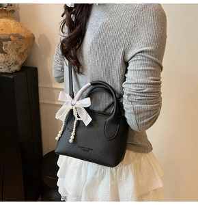 Detail of black pebbled leather bucket bag with silk bow and pearl charms worn by a model