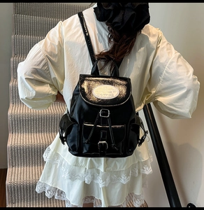 Detail of glossy black backpack featuring a flap closure and white logo on back of a model