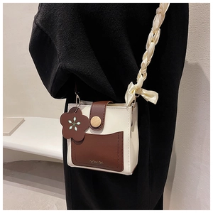 Detail of crossbody box bag with contrast strap and decorative floral charm accessory