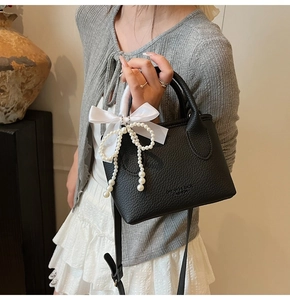 Detail of black lychee grain leather bucket bag with white pearl strings and silk bow knot