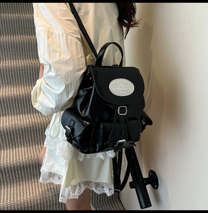 Close-up of black glossy PU backpack featuring drawstring closure and side buckle pockets
