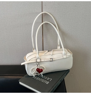 Close-up of white leather shoulder bag with decorative red heart and pearl charm detail