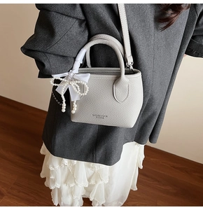 Close-up of light grey litchi grain leather bucket bag with pearl and ribbon bow charms