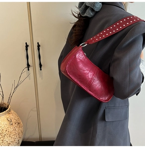Close-up of wine red baguette bag with wide silver studded shoulder strap and oil wax texture