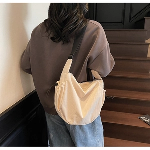 Detail of off-white canvas hobo bag with black drawstring and adjustable wide strap on a model