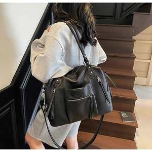 Detailed macro view of black pebbled leather tote bag with stylish tassels and metal zippers