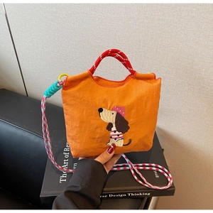 Detail of orange dachshund embroidered bag with red rope handles and woven strap