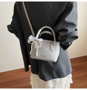 Detail of light gray lychee grain leather bag with pearl tassel and white ribbon bow
