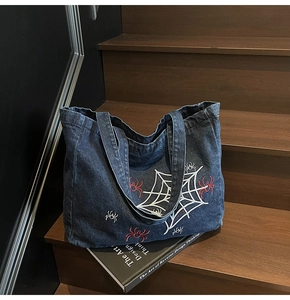 Detail of vintage gothic spider web embroidery on dark blue denim tote bag with red spiders