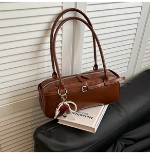 Detail view of brown Boston bag with smooth leather finish and a pearl heart pendant