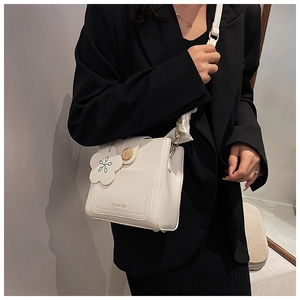 Detail of white PU leather crossbody bag with flower charm and logo on a model