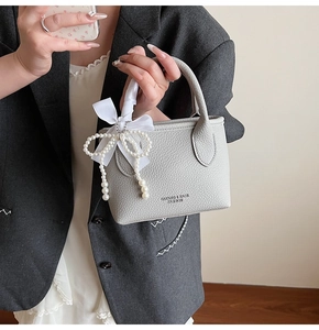 Detail of grey lychee leather bucket bag with pearl pendant and silk bow handle