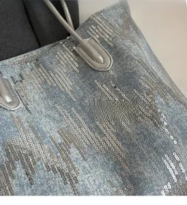 Close-up of light blue washed denim tote bag with shiny silver sequins and gray strap