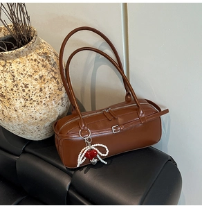 Detail of vintage brown Boston pillow bag with pearl heart pendant on black cushion