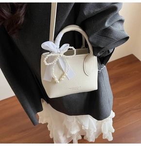 Detail of a creamy white leather mini bucket bag with satin bow and pearl heart decoration