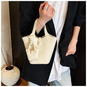 Detail of cream lychee leather bucket bag featuring a matching mini charm and buckle closure