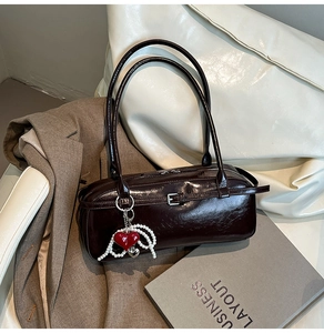 Detail of burgundy leather shoulder bag with decorative heart and pearl charm